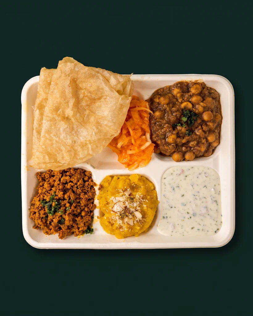 Weekend Halwa Puri Nashta tray — puri, chana, chicken qeema, suji halwa, pickled onions and raita, studio-shot on emerald